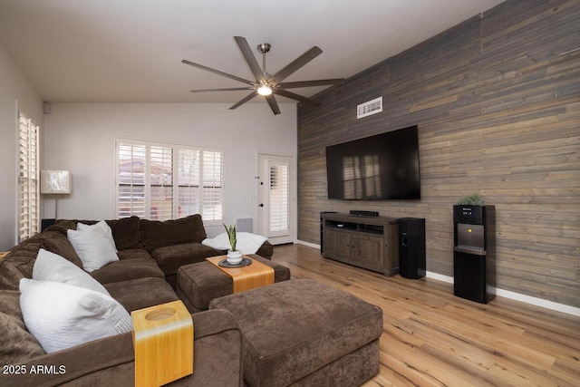 living room with ceiling fan, high vaulted ceiling, light hardwood / wood-style floors, and wood walls