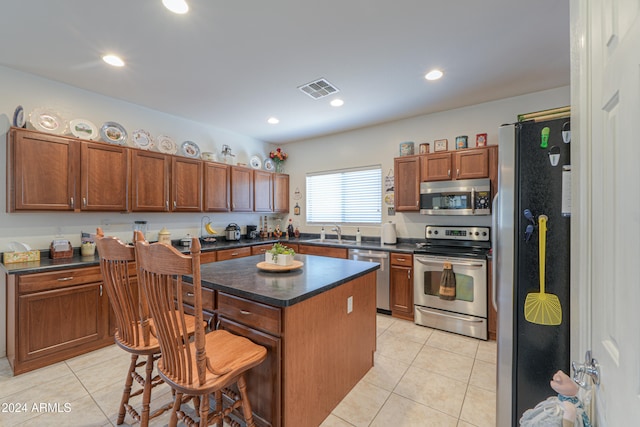 kitchen featuring light tile patterned flooring, sink, appliances with stainless steel finishes, a kitchen island, and a kitchen bar