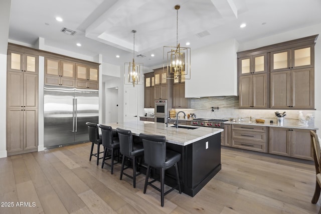 kitchen with light stone countertops, appliances with stainless steel finishes, an island with sink, sink, and hanging light fixtures