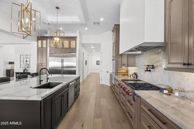 kitchen with premium range hood, appliances with stainless steel finishes, light stone countertops, pendant lighting, and sink