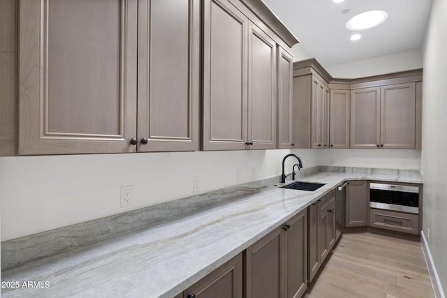 kitchen with light stone countertops, sink, oven, and light hardwood / wood-style floors