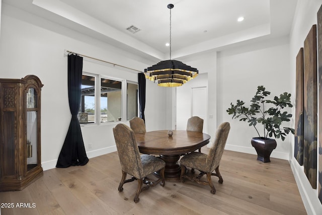 dining area with a tray ceiling and light hardwood / wood-style flooring