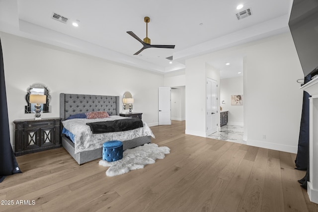 bedroom with ceiling fan, ensuite bath, a raised ceiling, and light hardwood / wood-style floors