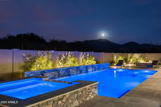 pool at twilight featuring pool water feature and an in ground hot tub