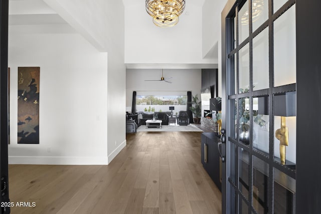 foyer entrance with ceiling fan with notable chandelier, a high ceiling, and wood-type flooring