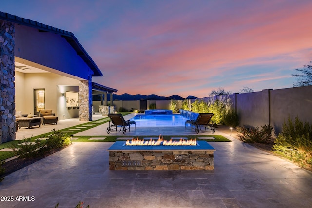 patio terrace at dusk featuring an outdoor fire pit and a fenced in pool