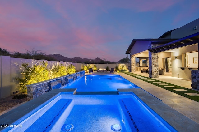 pool at dusk featuring a patio area, outdoor lounge area, and an in ground hot tub