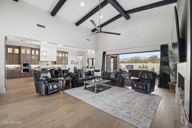 living room with light hardwood / wood-style flooring, ceiling fan with notable chandelier, high vaulted ceiling, and beamed ceiling