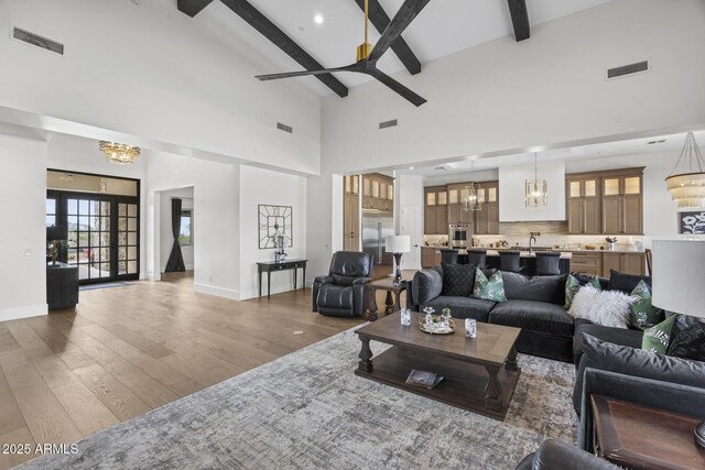 living room featuring ceiling fan with notable chandelier, a high ceiling, dark hardwood / wood-style flooring, and beamed ceiling