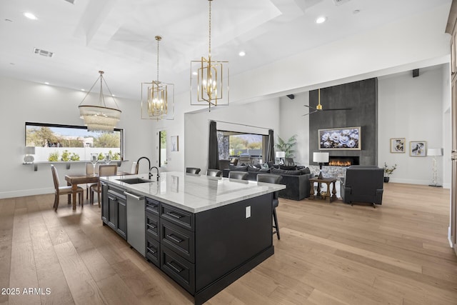 kitchen with an island with sink, light hardwood / wood-style floors, sink, hanging light fixtures, and a fireplace