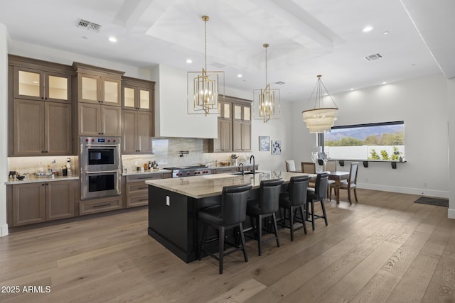 kitchen with a center island with sink, stainless steel appliances, hanging light fixtures, light stone counters, and a breakfast bar