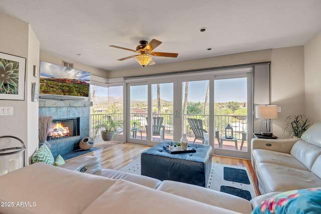 living room with a wealth of natural light, wood finished floors, a ceiling fan, and a tile fireplace