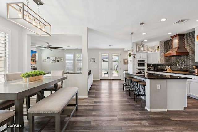 20518 W White Rock Rd, Buckeye, AZ 85396 - kitchen with wall chimney range hood, dark wood-type flooring, dark countertops, a kitchen island with sink, and ceiling fan