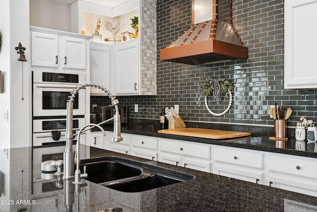 20518 W White Rock Rd, Buckeye, AZ 85396 - kitchen featuring wall chimney range hood, white double oven, backsplash, white cabinets, and dark stone counters