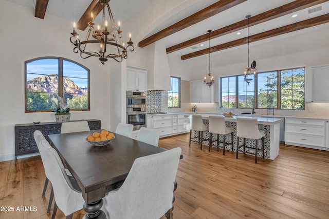 dining space with an inviting chandelier, a towering ceiling, beam ceiling, and light wood-type flooring