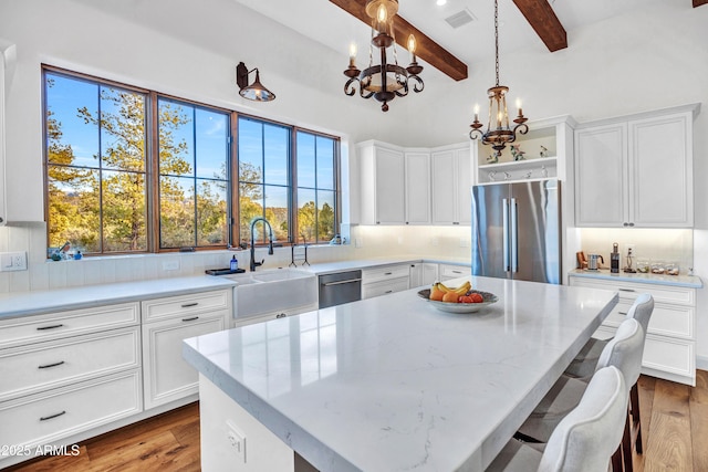 kitchen featuring sink, hanging light fixtures, appliances with stainless steel finishes, a kitchen island, and light stone countertops