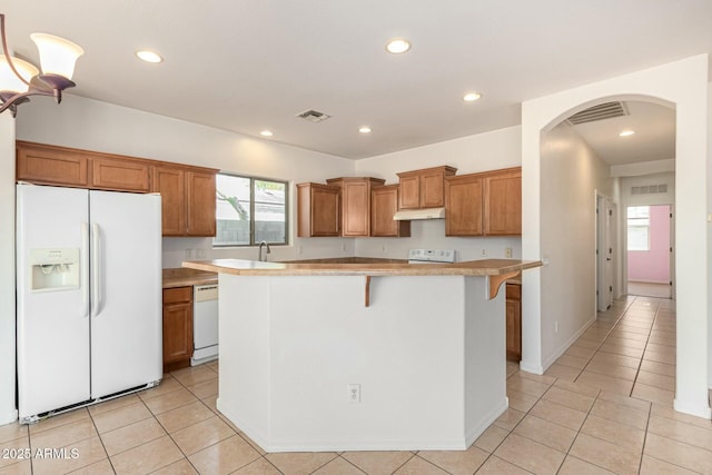 kitchen featuring a breakfast bar, sink, a center island, light tile patterned floors, and white appliances