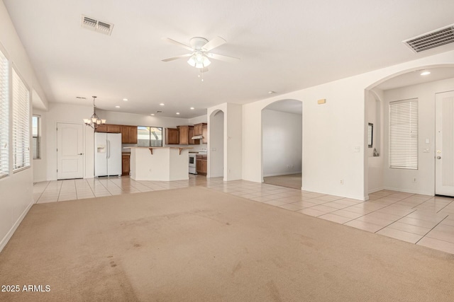 unfurnished living room featuring ceiling fan with notable chandelier and light carpet