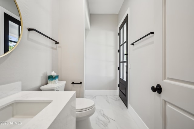 bathroom featuring marble look tile flooring, vanity, toilet, and baseboards