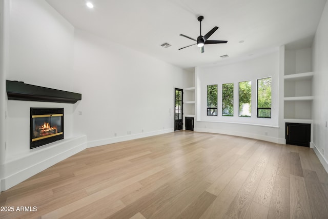 unfurnished living room with a glass covered fireplace, built in shelves, ceiling fan, light wood-style floors, and recessed lighting