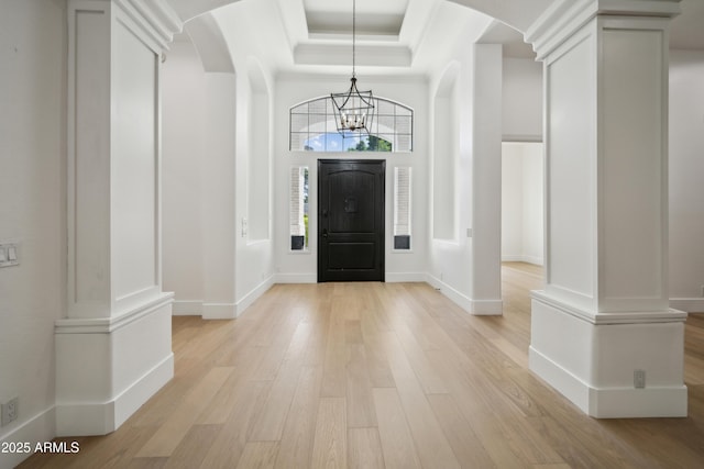foyer featuring a chandelier, light wood-style floors, arched walkways, and a raised ceiling