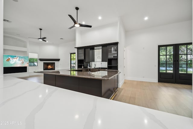 kitchen featuring light wood-type flooring, a lit fireplace, ceiling fan, a large island with sink, and recessed lighting