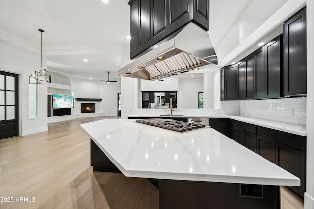 kitchen featuring stainless steel gas stovetop, dark cabinets, open floor plan, a center island, and light wood-type flooring