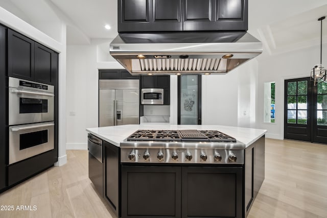 kitchen with built in appliances, wall chimney range hood, light wood-style flooring, light stone countertops, and recessed lighting