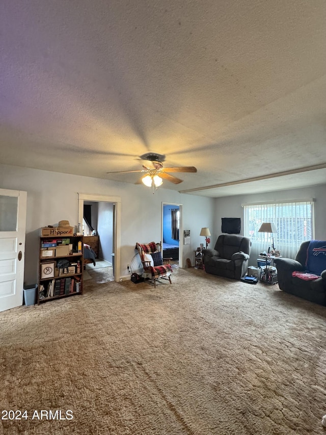 living room with carpet floors, a ceiling fan, and a textured ceiling
