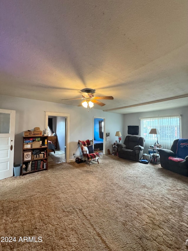 living room with ceiling fan, a textured ceiling, and carpet