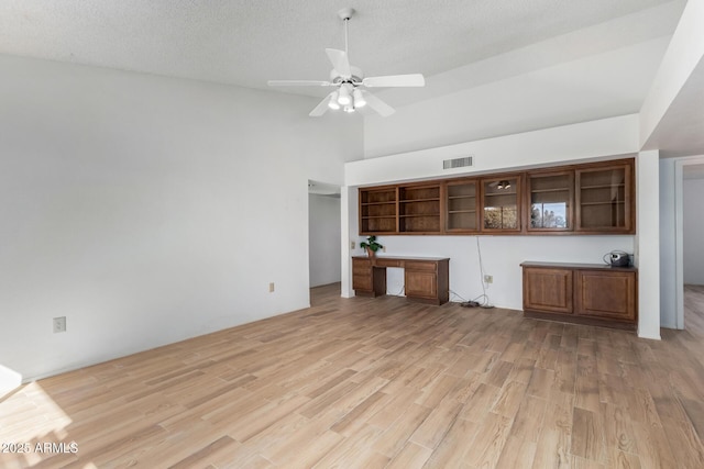 unfurnished living room featuring ceiling fan, a textured ceiling, built in desk, and light wood-type flooring