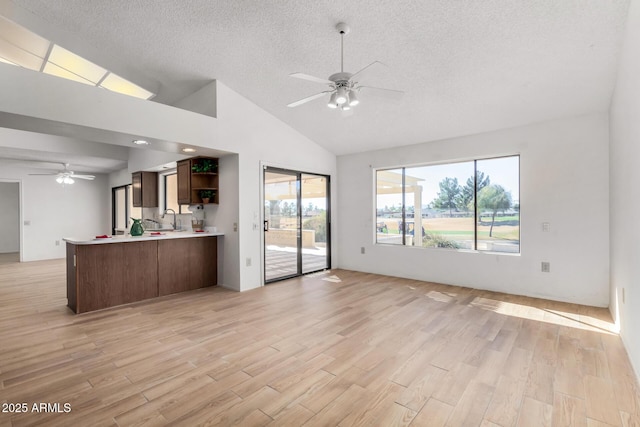 unfurnished living room featuring ceiling fan, vaulted ceiling, sink, light wood-type flooring, and a textured ceiling