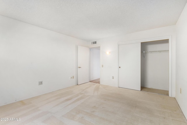 unfurnished bedroom featuring a textured ceiling, a closet, and light colored carpet