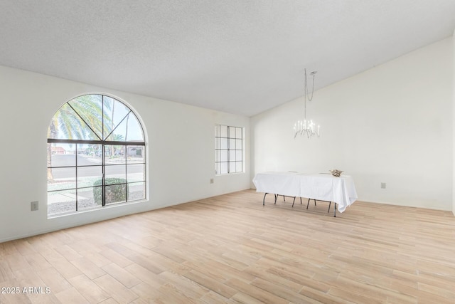 unfurnished bedroom with lofted ceiling, a notable chandelier, a textured ceiling, and light hardwood / wood-style flooring