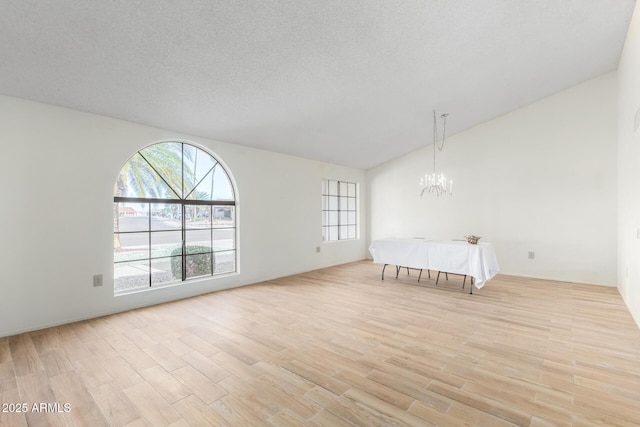 unfurnished bedroom with a textured ceiling, light hardwood / wood-style flooring, lofted ceiling, and an inviting chandelier