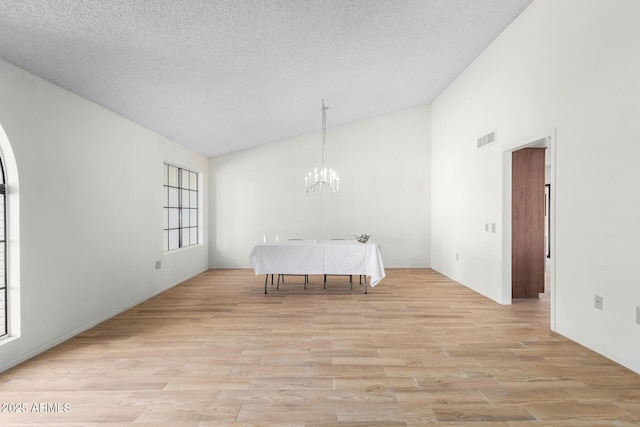 dining room featuring light wood-type flooring, a chandelier, a textured ceiling, and high vaulted ceiling