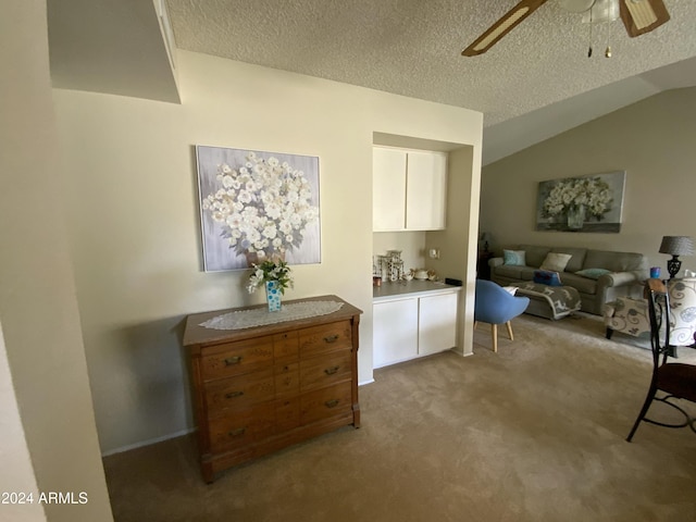 interior space featuring a textured ceiling, white cabinetry, light colored carpet, and vaulted ceiling