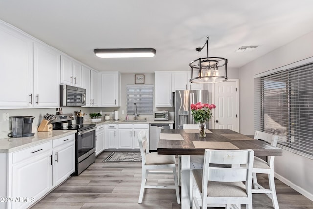 kitchen featuring sink, white cabinetry, light stone counters, decorative light fixtures, and stainless steel appliances