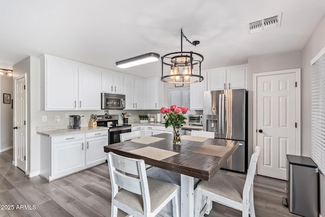 kitchen with appliances with stainless steel finishes, white cabinetry, hanging light fixtures, a notable chandelier, and light hardwood / wood-style floors