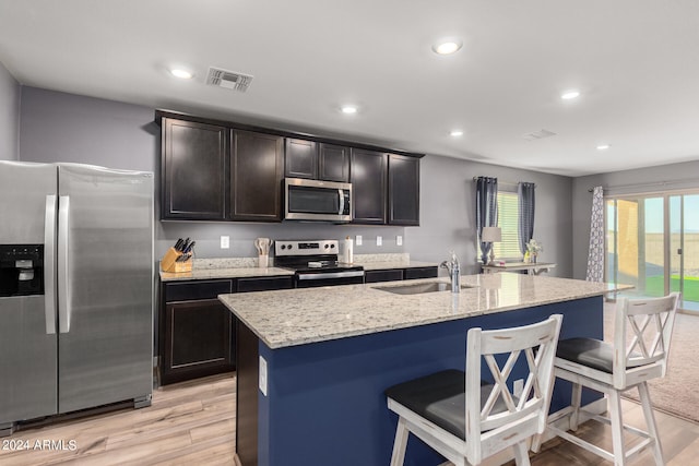 kitchen with an island with sink, sink, stainless steel appliances, and light hardwood / wood-style flooring