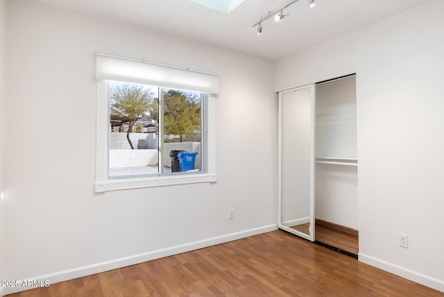 unfurnished bedroom featuring a skylight, a closet, baseboards, and wood finished floors