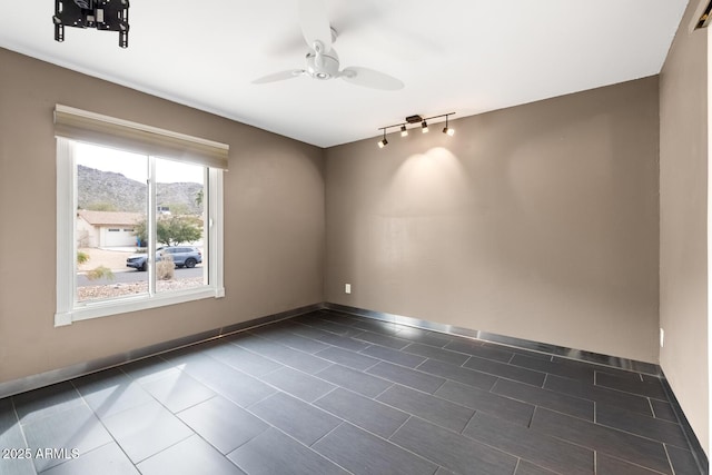 empty room with dark tile patterned floors, ceiling fan, baseboards, and rail lighting