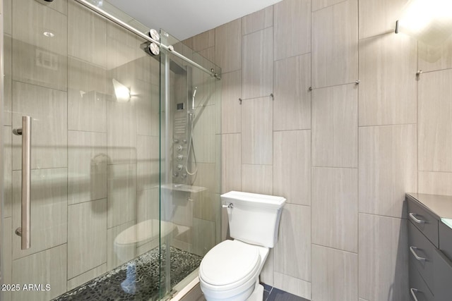 full bath with a stall shower, vanity, toilet, and tile walls