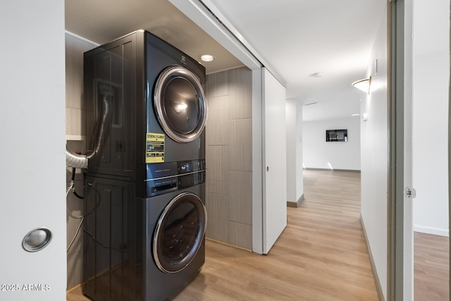 laundry room with laundry area, light wood-style flooring, stacked washer and clothes dryer, and baseboards