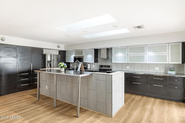 kitchen with a skylight, visible vents, wall chimney exhaust hood, modern cabinets, and appliances with stainless steel finishes