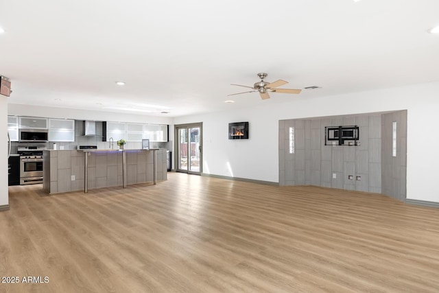 unfurnished living room with visible vents, a sink, ceiling fan, light wood-type flooring, and baseboards