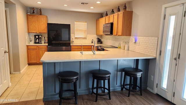 kitchen with decorative backsplash, sink, kitchen peninsula, black fridge, and a breakfast bar area