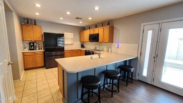 kitchen with kitchen peninsula, sink, backsplash, black appliances, and a breakfast bar area