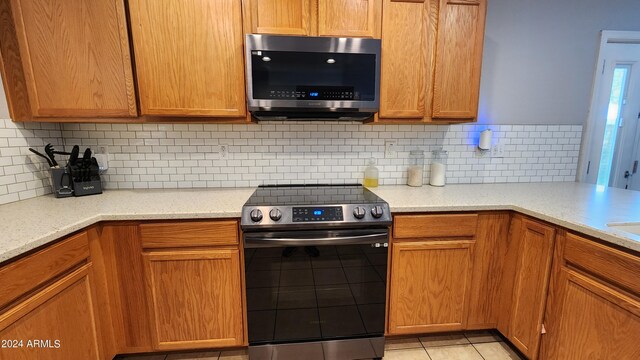 kitchen featuring light stone countertops, backsplash, appliances with stainless steel finishes, and light tile patterned flooring