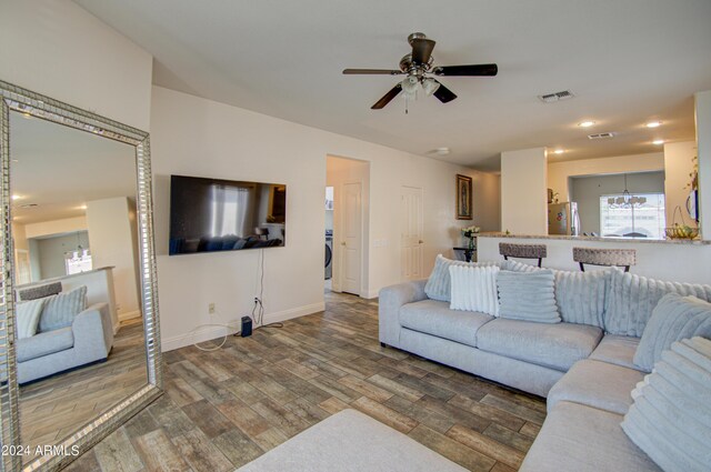 living room featuring ceiling fan with notable chandelier, washer / clothes dryer, visible vents, wood finished floors, and baseboards